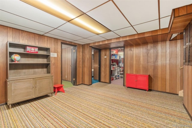 interior space featuring a paneled ceiling, light carpet, and wooden walls