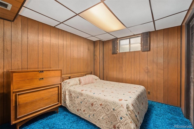 carpeted bedroom with wooden walls and a drop ceiling