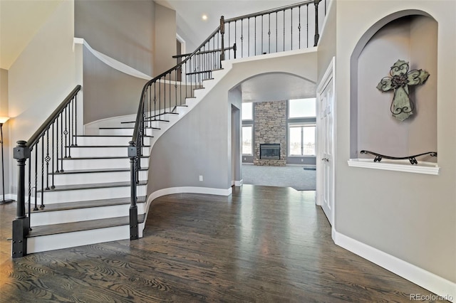 foyer entrance featuring dark hardwood / wood-style floors, a stone fireplace, and a high ceiling