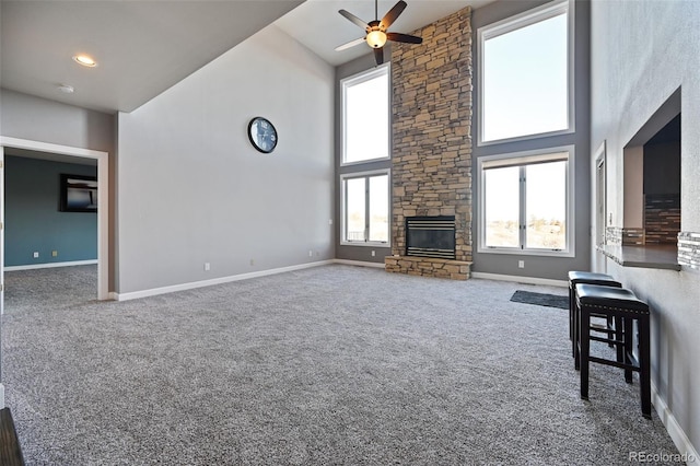 unfurnished living room with ceiling fan, a fireplace, carpet, and a high ceiling