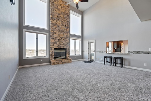 unfurnished living room featuring carpet floors, ceiling fan, a fireplace, and a towering ceiling