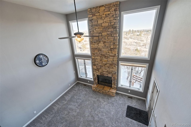 unfurnished living room with dark carpet, a high ceiling, a stone fireplace, and ceiling fan