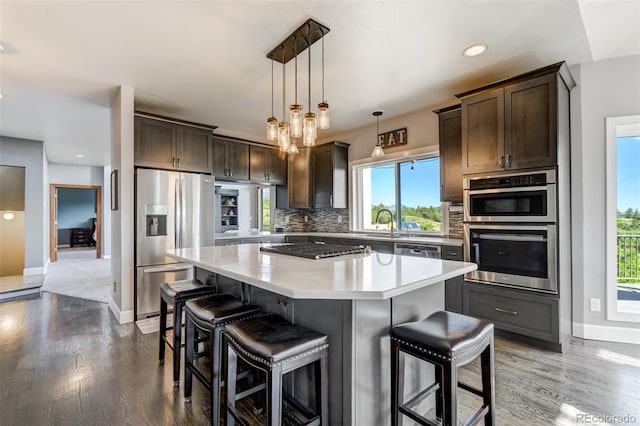 kitchen featuring appliances with stainless steel finishes, tasteful backsplash, dark brown cabinets, decorative light fixtures, and a kitchen island