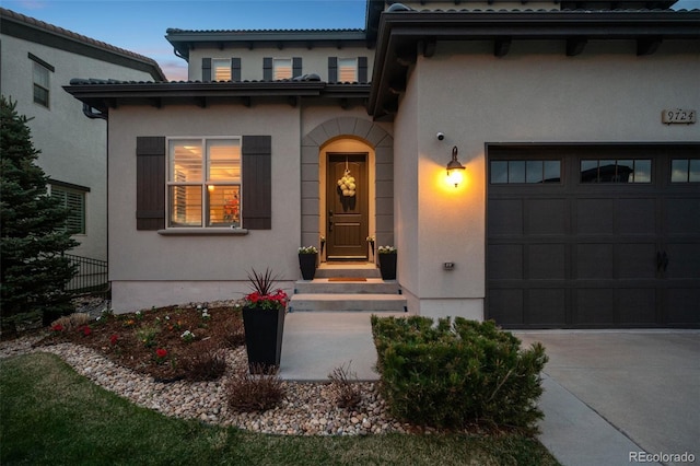 property entrance featuring stucco siding, an attached garage, driveway, and fence
