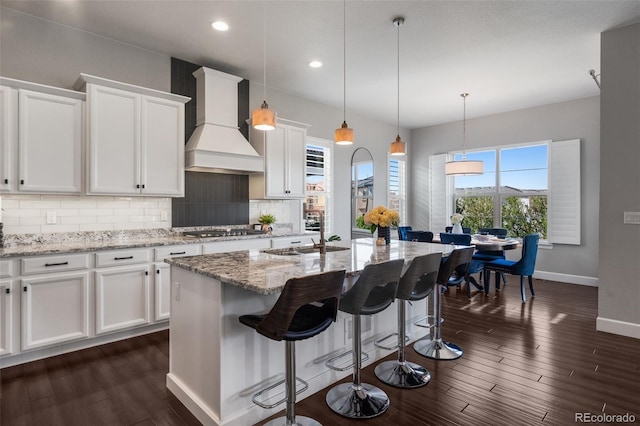 kitchen with tasteful backsplash, stainless steel gas cooktop, premium range hood, dark wood finished floors, and baseboards