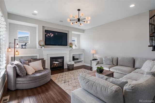 living area featuring recessed lighting, dark wood-style floors, visible vents, a glass covered fireplace, and a notable chandelier