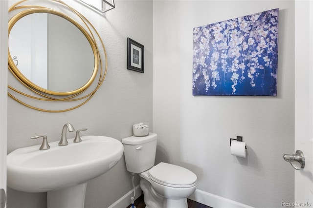 half bathroom featuring toilet, baseboards, and a sink