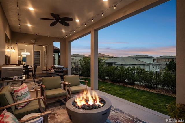patio terrace at dusk featuring ceiling fan, a fenced backyard, and a fire pit