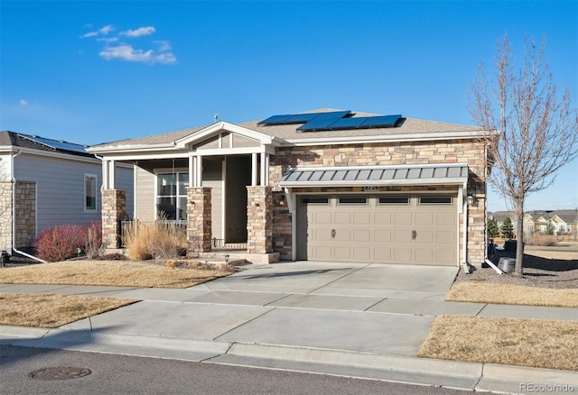 view of front facade with a shingled roof, covered porch, concrete driveway, roof mounted solar panels, and stone siding