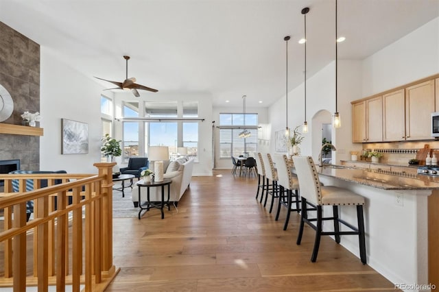 kitchen with arched walkways, a fireplace, a sink, light wood-type flooring, and a kitchen bar