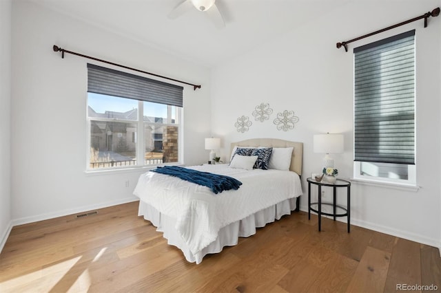 bedroom featuring a ceiling fan, wood finished floors, visible vents, and baseboards