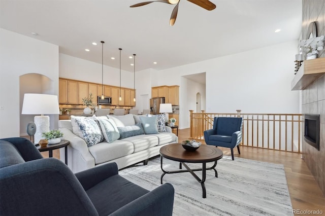 living area featuring arched walkways, light wood finished floors, a towering ceiling, and recessed lighting