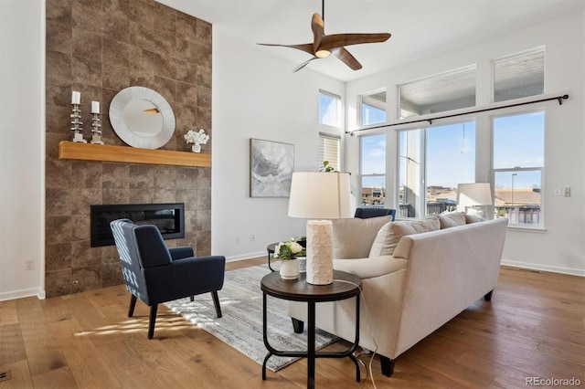 living room with ceiling fan, a fireplace, baseboards, and wood finished floors