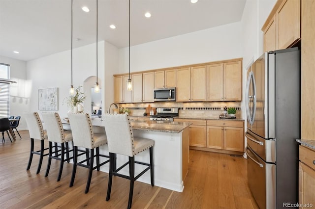 kitchen featuring appliances with stainless steel finishes, light brown cabinets, decorative backsplash, and wood finished floors