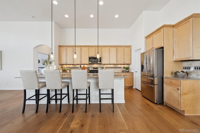 kitchen with stainless steel appliances, light brown cabinets, a towering ceiling, and a kitchen breakfast bar