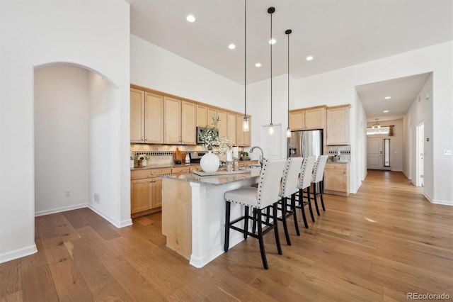 kitchen featuring stainless steel appliances, arched walkways, decorative backsplash, and light brown cabinetry