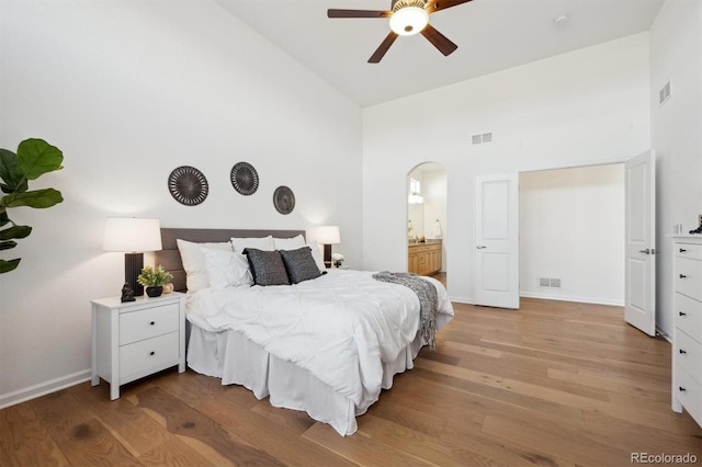 bedroom with visible vents, arched walkways, baseboards, light wood-style flooring, and high vaulted ceiling