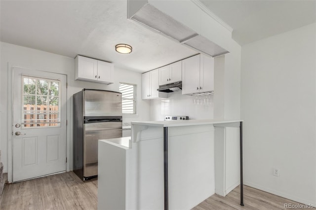 3281 S Estes St, Lakewood, CO 80227 - kitchen with freestanding refrigerator, under cabinet range hood, white cabinets, light wood-type flooring, and a peninsula