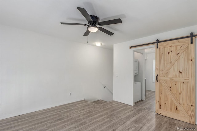 3281 S Estes St, Lakewood, CO 80227 - spare room featuring a barn door, stacked washing machine and dryer, ceiling fan, and light wood-type flooring