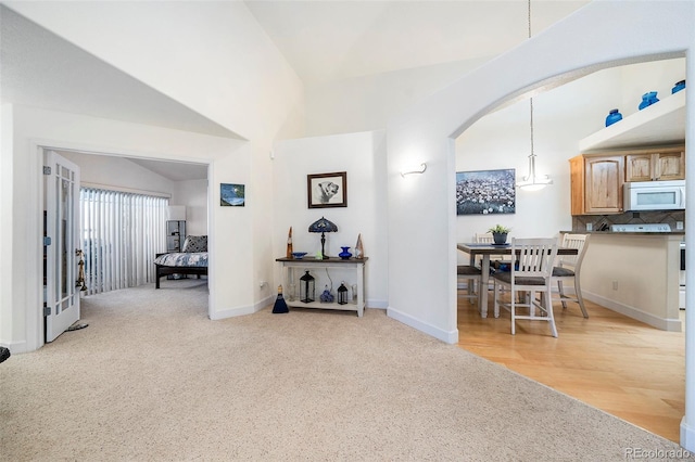 corridor with arched walkways, light carpet, vaulted ceiling, and baseboards