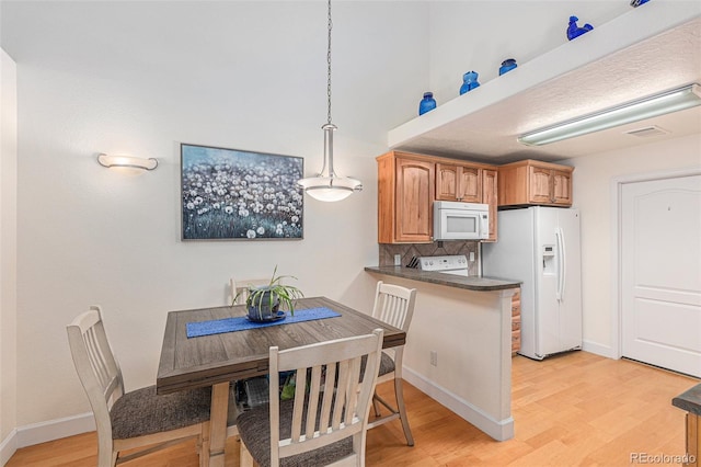 kitchen with light wood finished floors, white appliances, dark countertops, and backsplash