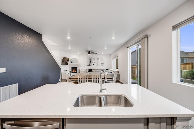 16673 E Virginia Ave, Aurora, CO 80017 - kitchen featuring a sink, open floor plan, ceiling fan, a lit fireplace, and a center island with sink