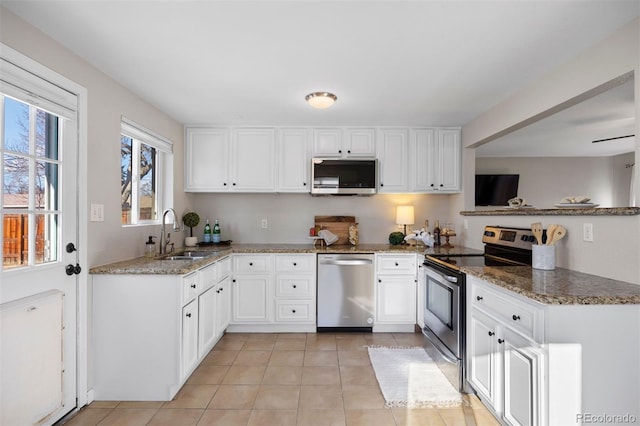 kitchen featuring stainless steel appliances, light tile patterned floors, white cabinets, dark stone counters, and sink