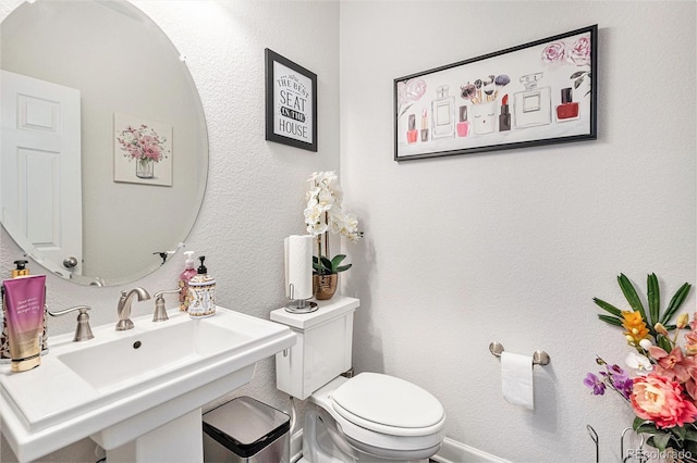 half bathroom featuring toilet, a textured wall, and a sink