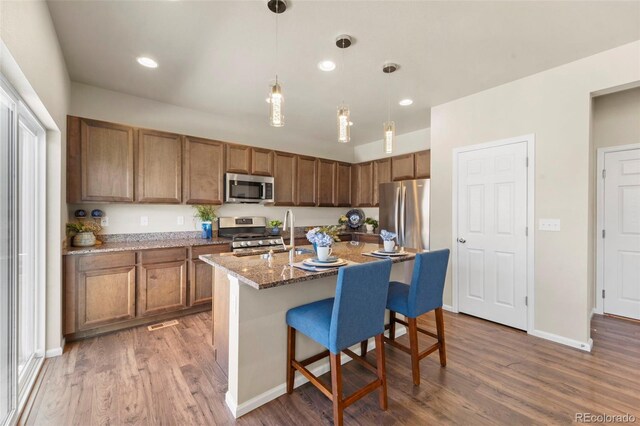 19131 E 65th Ave, Denver, CO 80249 - kitchen with appliances with stainless steel finishes, wood finished floors, a kitchen bar, brown cabinets, and recessed lighting