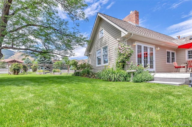 view of property exterior featuring a shingled roof, a chimney, a lawn, and french doors