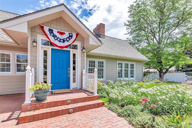 entrance to property featuring a shingled roof, fence, and a chimney