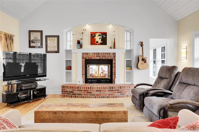 living area featuring built in features, lofted ceiling, a brick fireplace, and wood finished floors