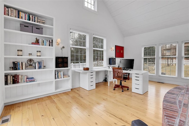 office area featuring high vaulted ceiling, built in shelves, light wood-type flooring, and visible vents