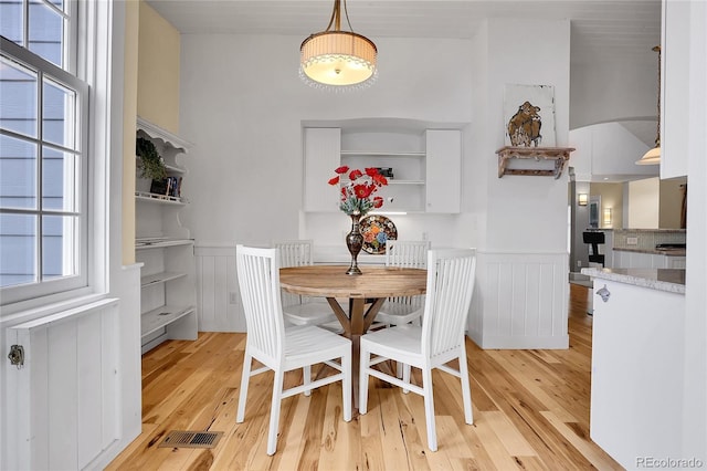 dining space with light wood-type flooring, a wainscoted wall, and visible vents