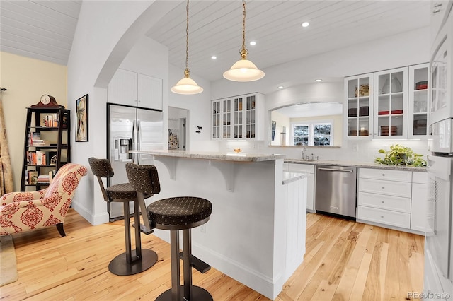 kitchen with arched walkways, stainless steel appliances, light wood-style floors, a sink, and a kitchen bar