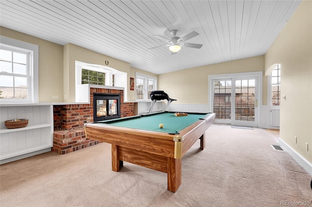 rec room featuring carpet floors, a healthy amount of sunlight, a brick fireplace, and wainscoting