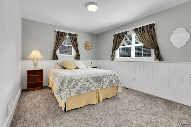 carpeted bedroom featuring a wainscoted wall and visible vents