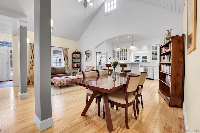 dining area featuring light wood-type flooring, a healthy amount of sunlight, and arched walkways