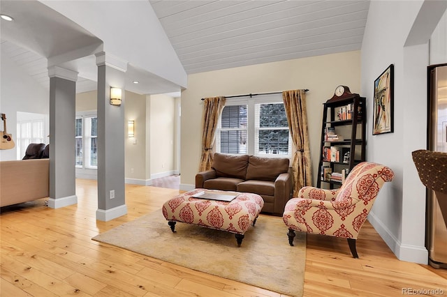 living area featuring lofted ceiling, light wood-style floors, baseboards, and ornate columns