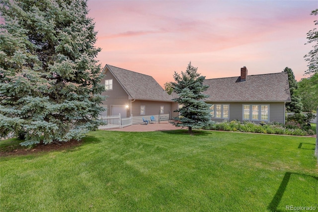 back of property at dusk featuring a patio area, a lawn, a chimney, and fence