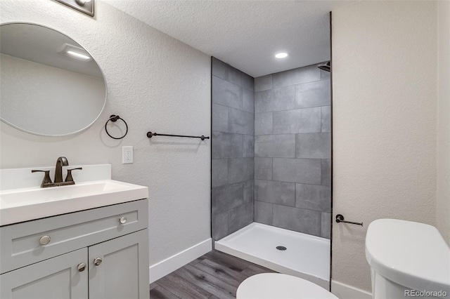 bathroom featuring toilet, baseboards, a tile shower, vanity, and wood finished floors