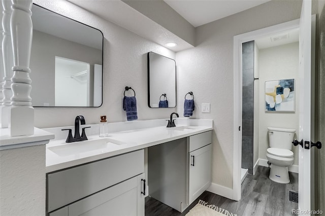 full bath with a sink, double vanity, toilet, and wood finished floors