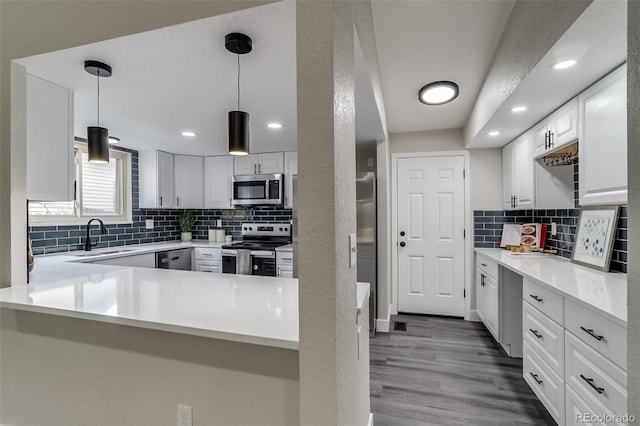 kitchen with wood finished floors, a sink, stainless steel appliances, light countertops, and decorative backsplash