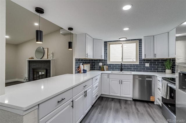kitchen with a peninsula, light wood-style flooring, a sink, stainless steel appliances, and backsplash