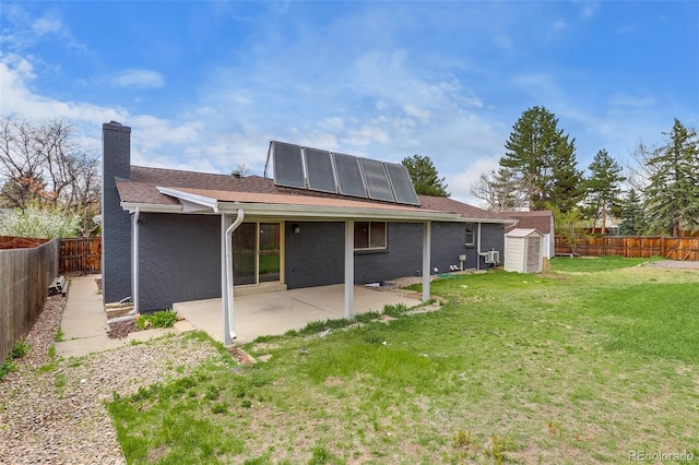 back of house with a storage shed, a patio, a fenced backyard, roof mounted solar panels, and a lawn
