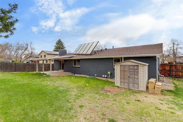 rear view of property with a yard, an outdoor structure, a patio area, a fenced backyard, and a storage unit