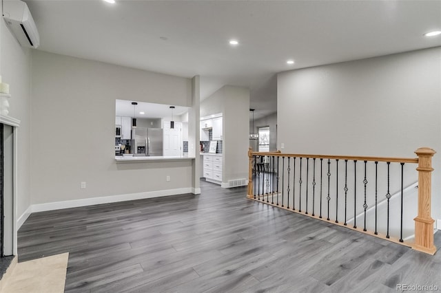 unfurnished living room featuring dark wood-style flooring, a wall mounted air conditioner, baseboards, and recessed lighting