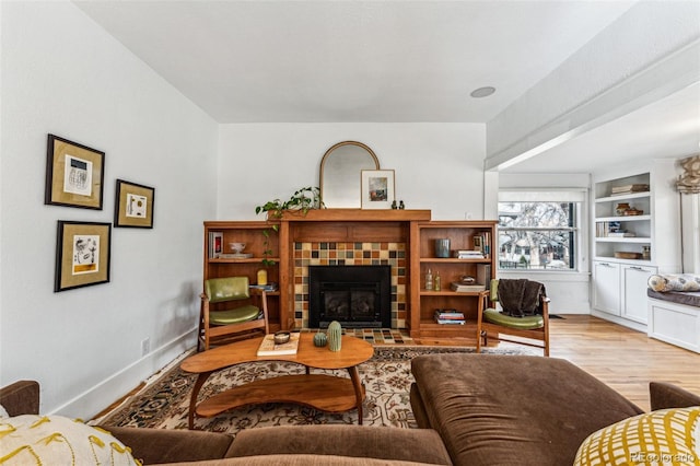 living room featuring built in shelves, a tiled fireplace, wood finished floors, and baseboards