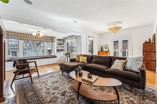 living room featuring built in features, french doors, a chandelier, and light wood-style flooring