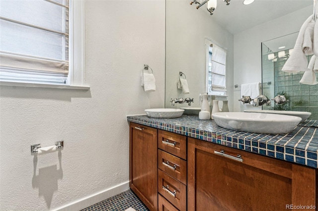 full bathroom with double vanity, a shower stall, baseboards, and a sink